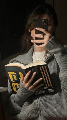 a woman is taking a selfie with her cell phone while holding a book in front of her face