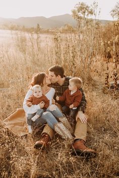 a family sitting in the grass with their two young children and one older man kissing each other