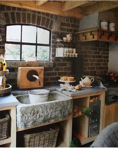 a kitchen with brick walls and stone sink in front of the window, surrounded by wicker baskets