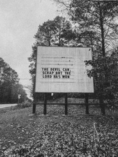 a large sign sitting on the side of a road in front of some tall trees