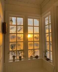 the sun shines through two windows in a room with potted plants on the window sill