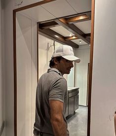 a man standing in front of a mirror wearing a white hat and grey t - shirt