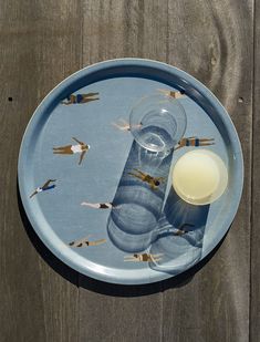 a blue plate topped with a glass filled with liquid next to a small candle on top of a wooden table