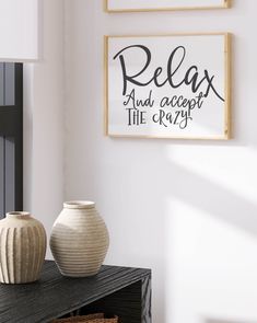 two vases are sitting on a table in front of a wall with some framed pictures