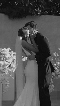 a bride and groom kissing in front of white flowers at their wedding ceremony, black and white photograph