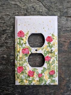 a painted light switch cover on a wooden surface with red and yellow flowers in the center