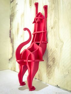 a red cat sculpture sitting on top of a white floor next to a wooden wall