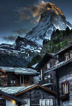 a mountain is in the distance behind some old wooden buildings with snow on them and dark clouds