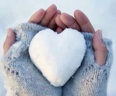 two hands holding a heart shaped pillow in the middle of their palm, with blurry background