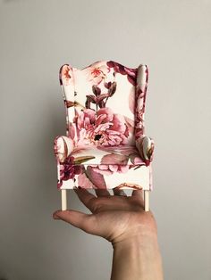 a hand holding up a miniature chair with flowers on it