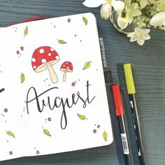 an open notebook with the word august written on it next to some pens and flowers