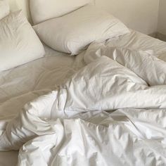 an unmade bed with white sheets and pillows