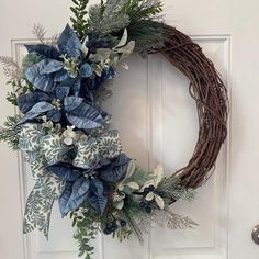 a wreath on the front door with blue and white flowers, greenery and leaves