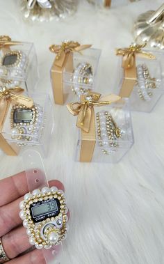 a hand holding a cell phone in front of four clear boxes with pearls and bows on them