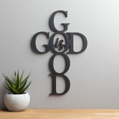 a metal sign that says god is good on the wall next to a potted plant