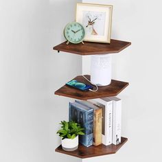 three shelves with books, plants and an alarm clock on each shelf in front of a white wall