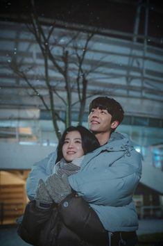 a man and woman standing next to each other in front of a building at night