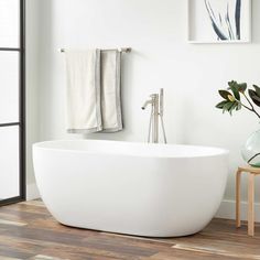 a white bath tub sitting on top of a wooden floor next to a vase filled with flowers