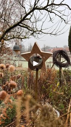 a wooden star sign sitting in the middle of a field next to some trees and bushes