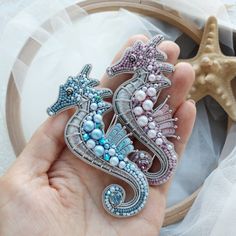 two seahorse brooches are being held by someone's hand