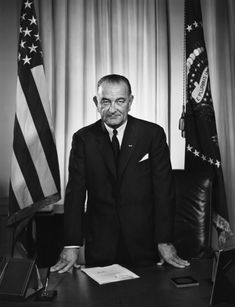 an old black and white photo of a man sitting at a desk in front of flags