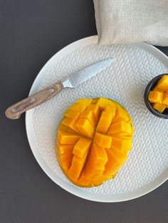 a white plate topped with a cut up mango next to a knife and bowl of fruit