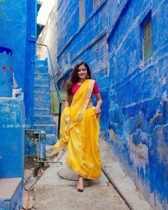 a woman in a yellow sari is walking down the street with blue buildings behind her