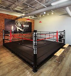 an empty boxing ring in the middle of a room with two benches and a poster on the wall