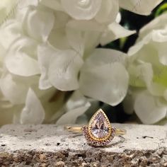 a close up of a ring on a rock with flowers in the background and water droplets