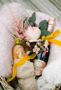 a basket filled with wine bottles and flowers on top of a wooden floor next to a blanket