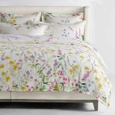 a bed with white linens and colorful flowers on the comforter, along with pillows