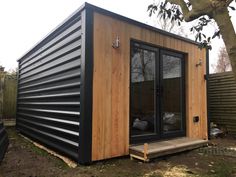 a small black and wood cabin with sliding glass doors on the outside, next to a tree