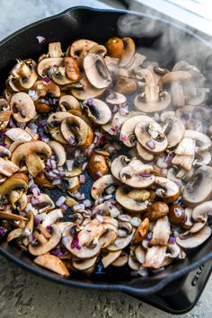 mushrooms and onions cooking in a skillet on top of a stove with steam coming out