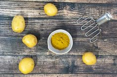 some yellow potatoes are in a white bowl with a whisk on the side