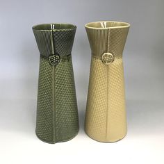 two vases sitting next to each other on a white tableclothed surface, one is green and the other is gold