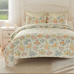 a bed with floral comforter and pillows in a room next to a white dresser