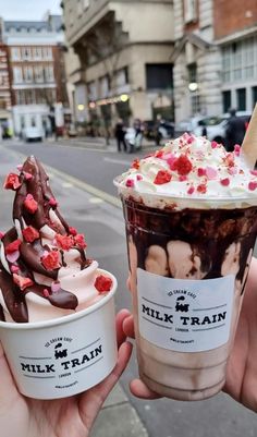 two people holding up ice cream and chocolate milkshakes in their hands on the street