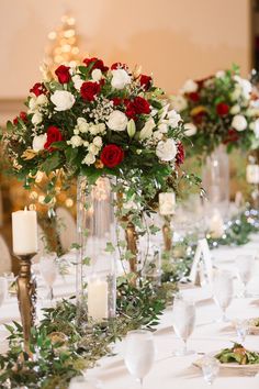 the table is set with white and red flowers, greenery, candles and silverware