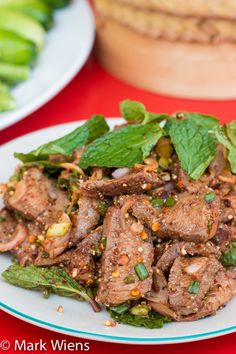 a white plate topped with meat covered in green leaves next to another plate filled with vegetables