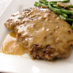 a white plate topped with meat covered in gravy and green beans