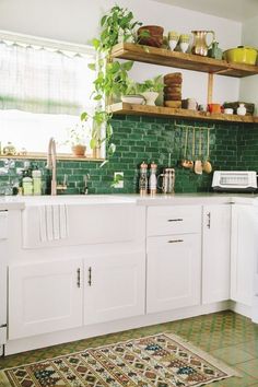 a kitchen with white cabinets and green tile backsplash, potted plants on the shelves