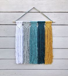 multicolored macrame wall hanging on white wooden planks with wood pegs