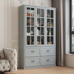 a white chair sitting in front of a gray china cabinet with glass doors and drawers