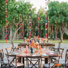 an outdoor table set up for a party with colorful beads hanging from the tree branches