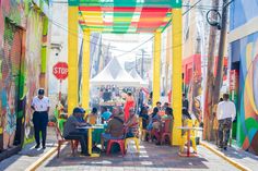 people sitting at tables in an alleyway with colorful walls and graffiti on the walls