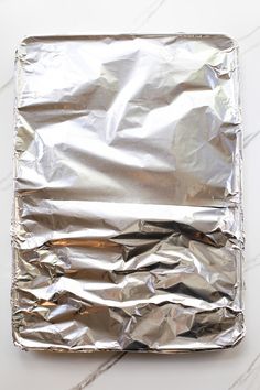 an aluminum foil covered square dish on a marble counter top, with the lid partially closed