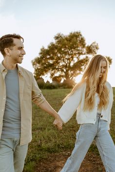 a man and woman holding hands walking through a field