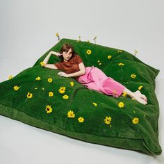 a woman laying on top of a green pillow with yellow flowers all over her body