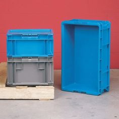 two plastic containers sitting on top of pallets in front of a red wall, one blue and the other gray