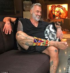 a man sitting on a couch with tattoos on his arms and legs, smiling at the camera